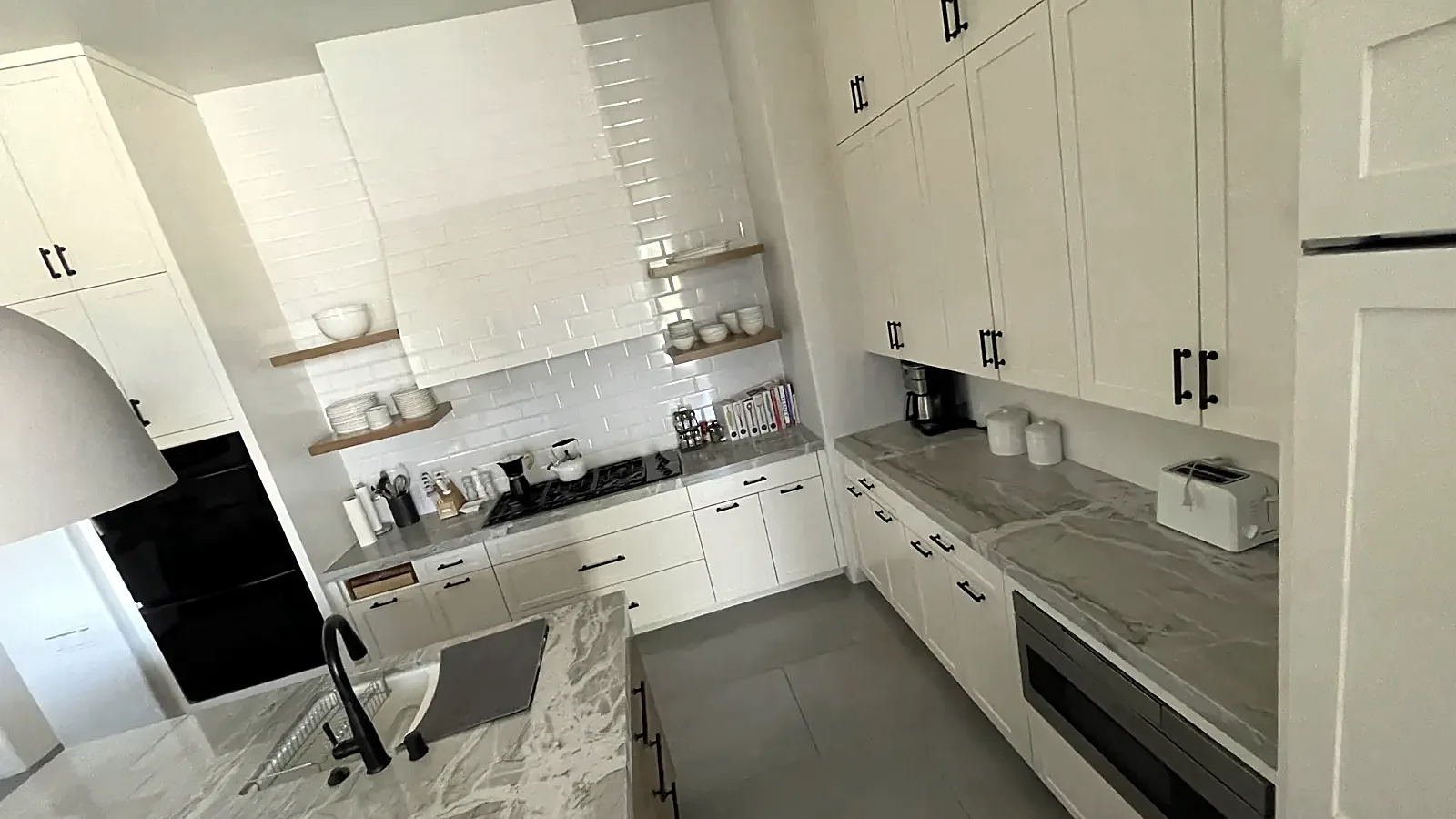 Finished white kitchen with grey marble counters, open shelves and black bar pulls