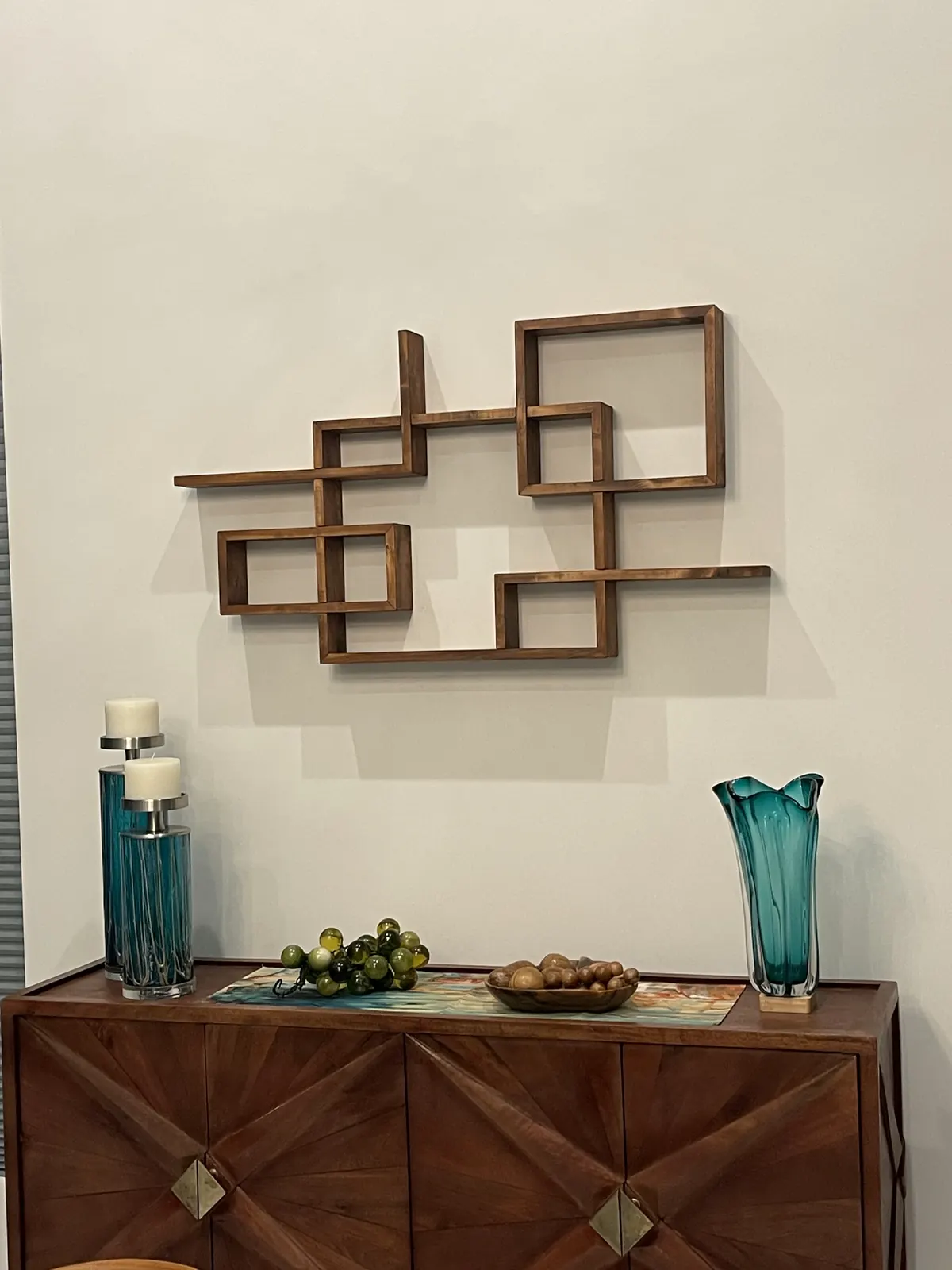 Geometric wood wall shelf centered above a console with art pieces