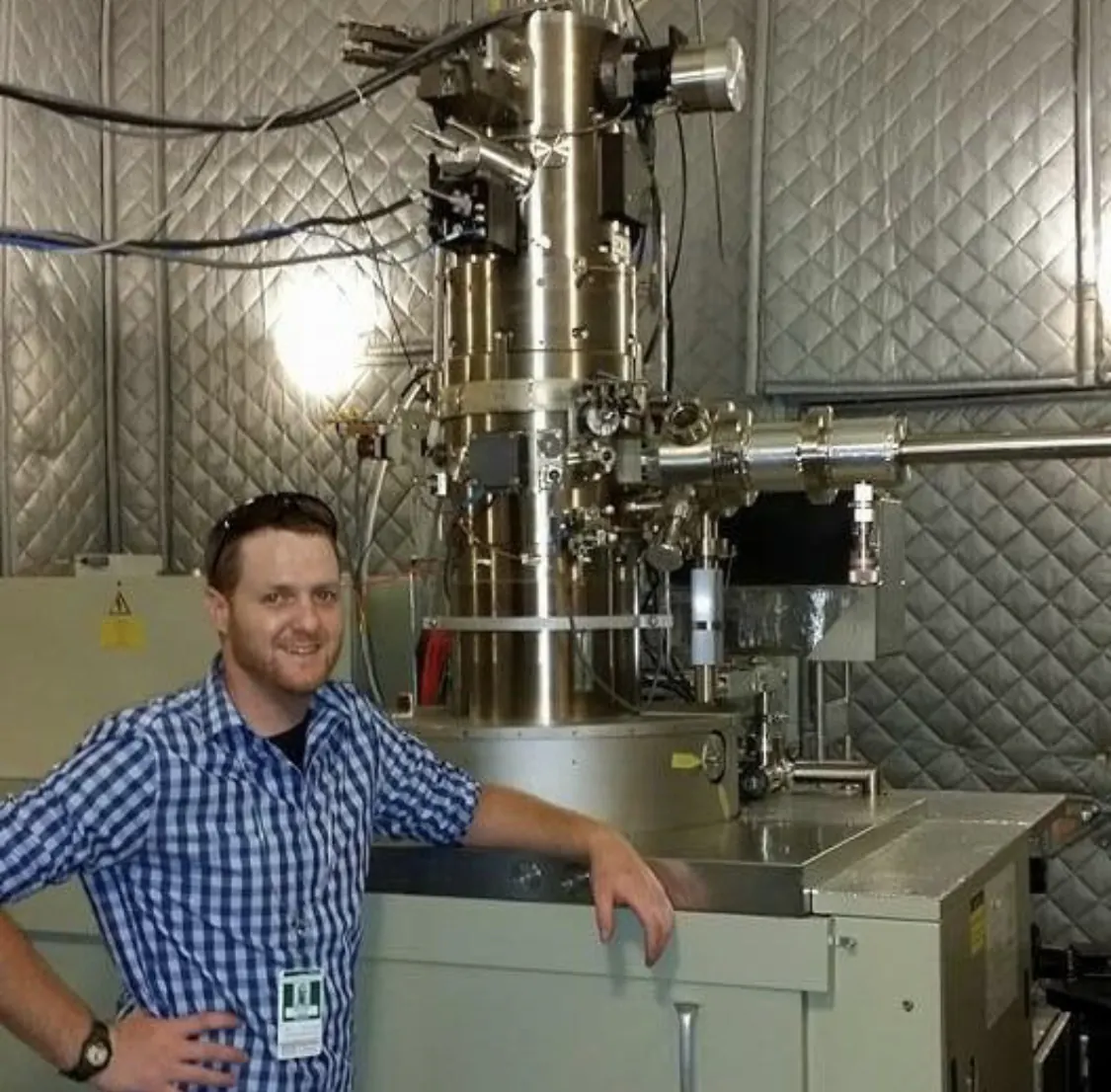 Owner beside an electron microscope column in a lab