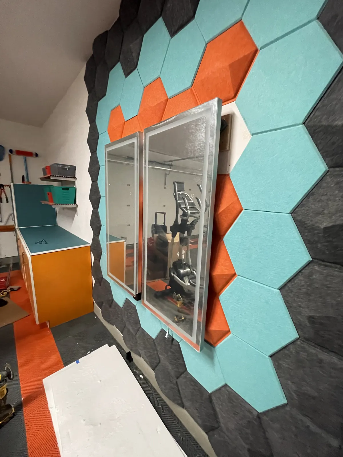 Wall mirror framed by teal, orange and black hexagon acoustic panels