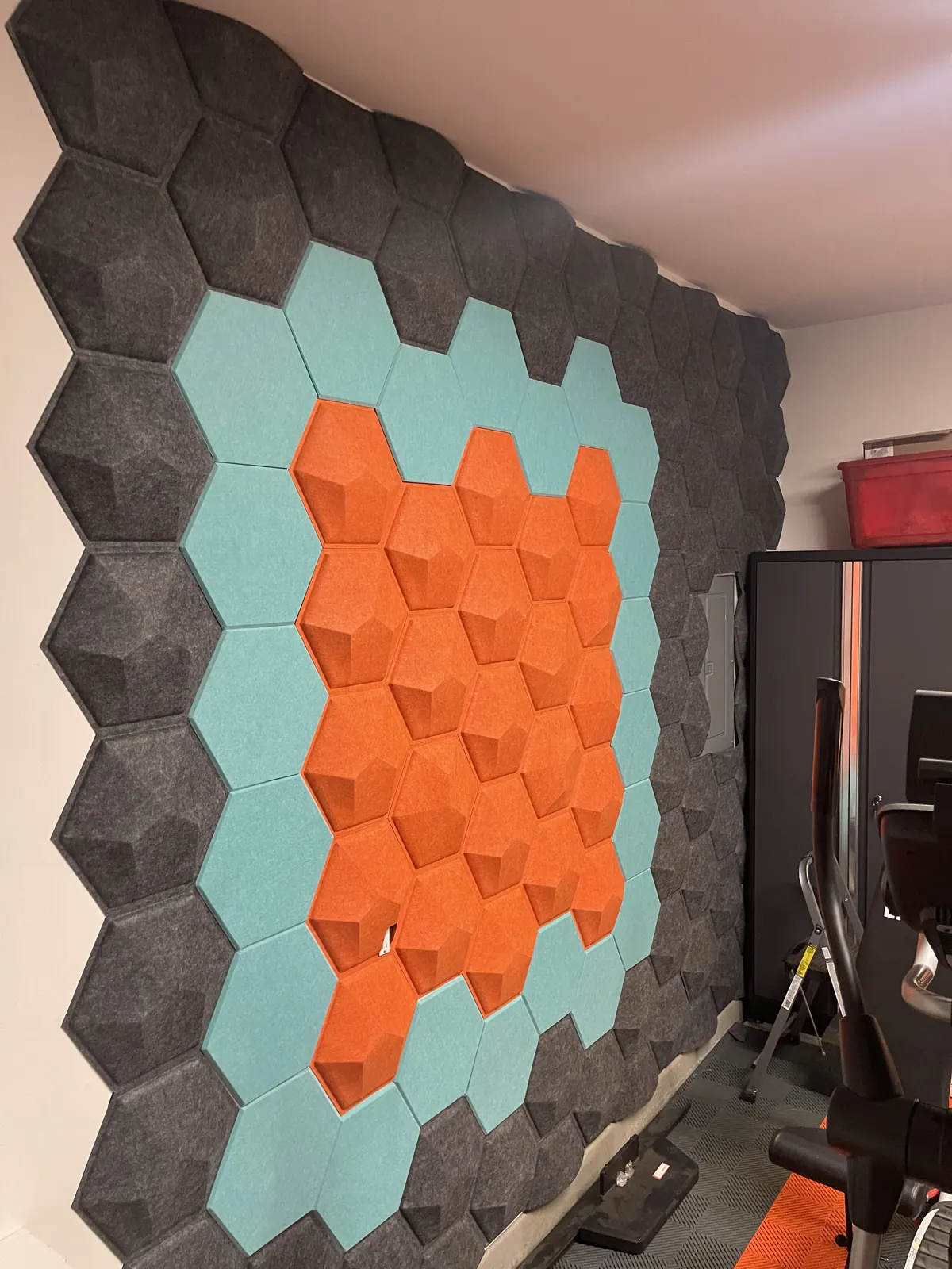 Hexagon acoustic panel wall in teal, orange and black around a mirror opening
