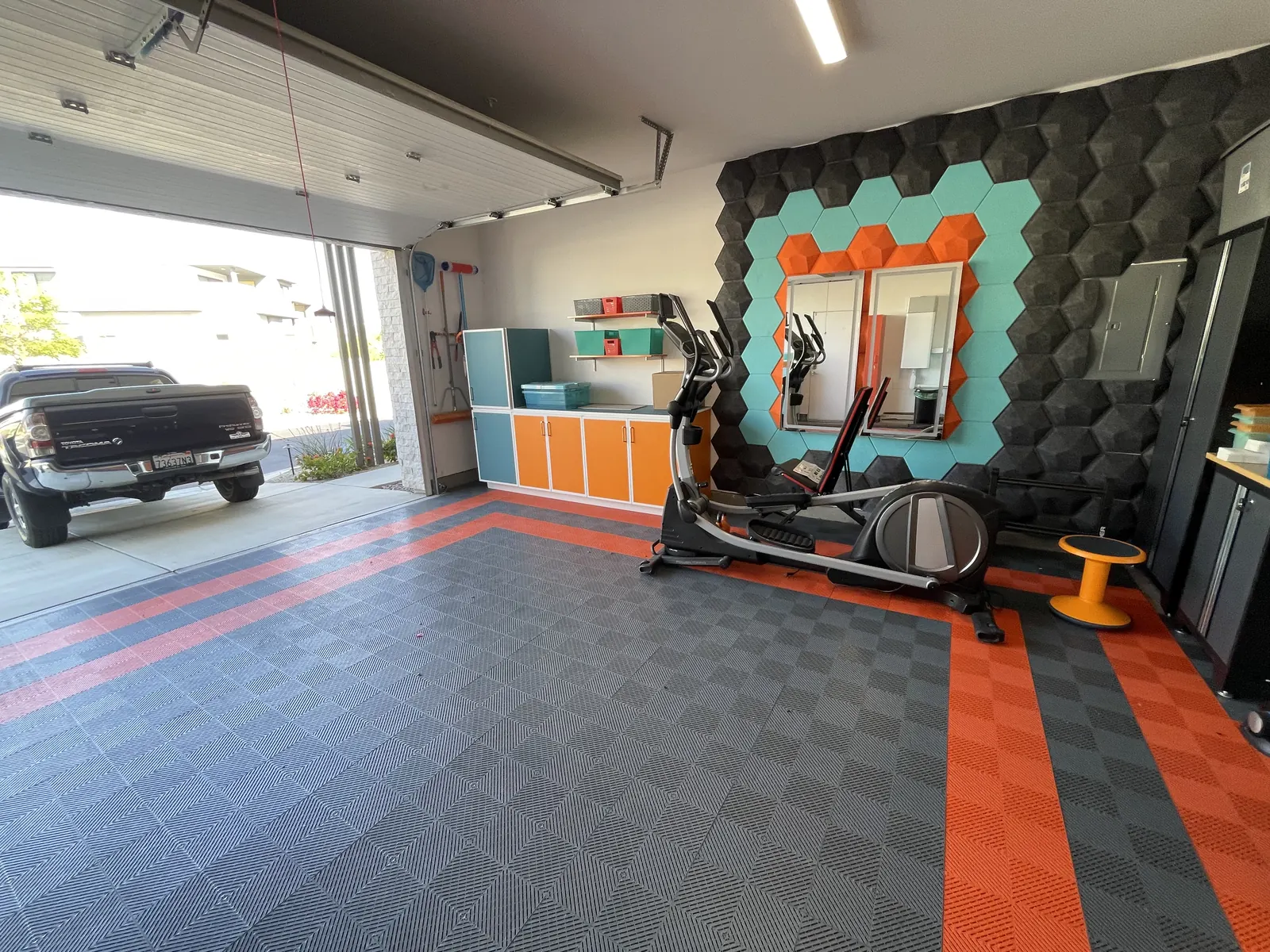 Finished garage gym seen from the driveway: orange and grey tile floor, hexagon acoustic wall and cabinets